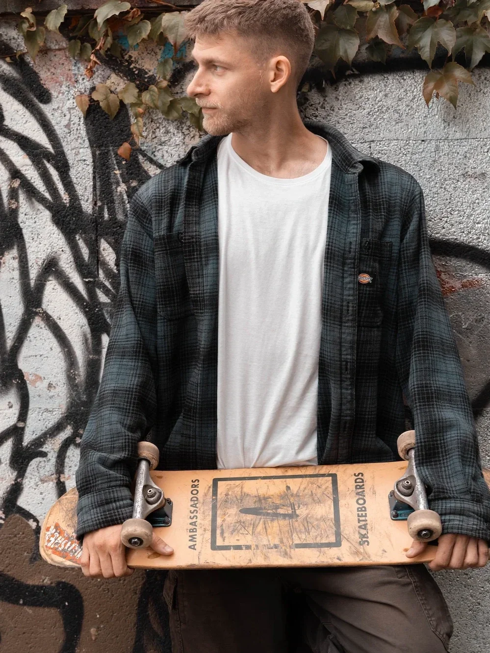 David Micev drží skateboard u zdi s graffiti