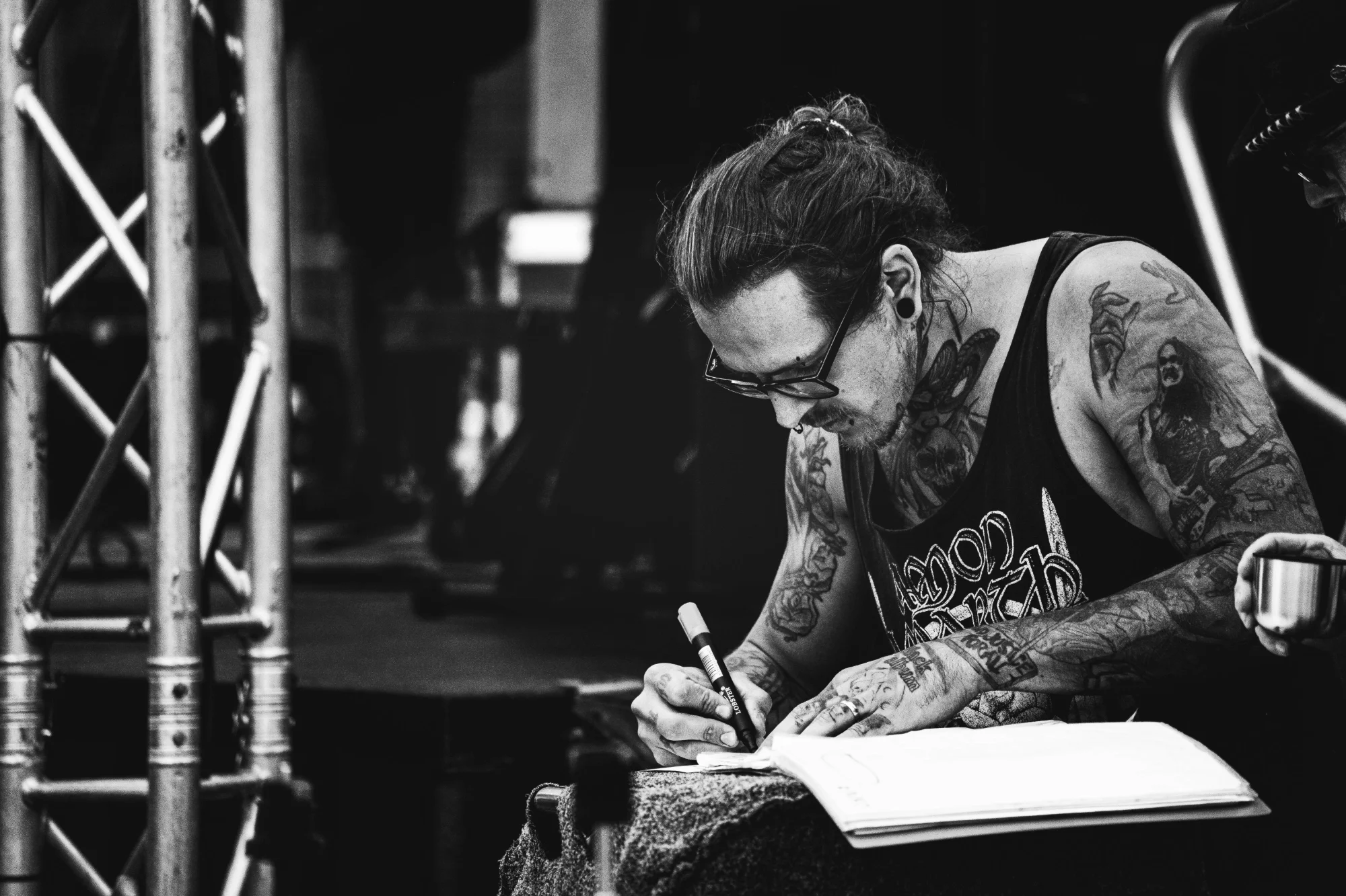 Potetovaný hudebník podepisuje setlist v zákulisí koncertu